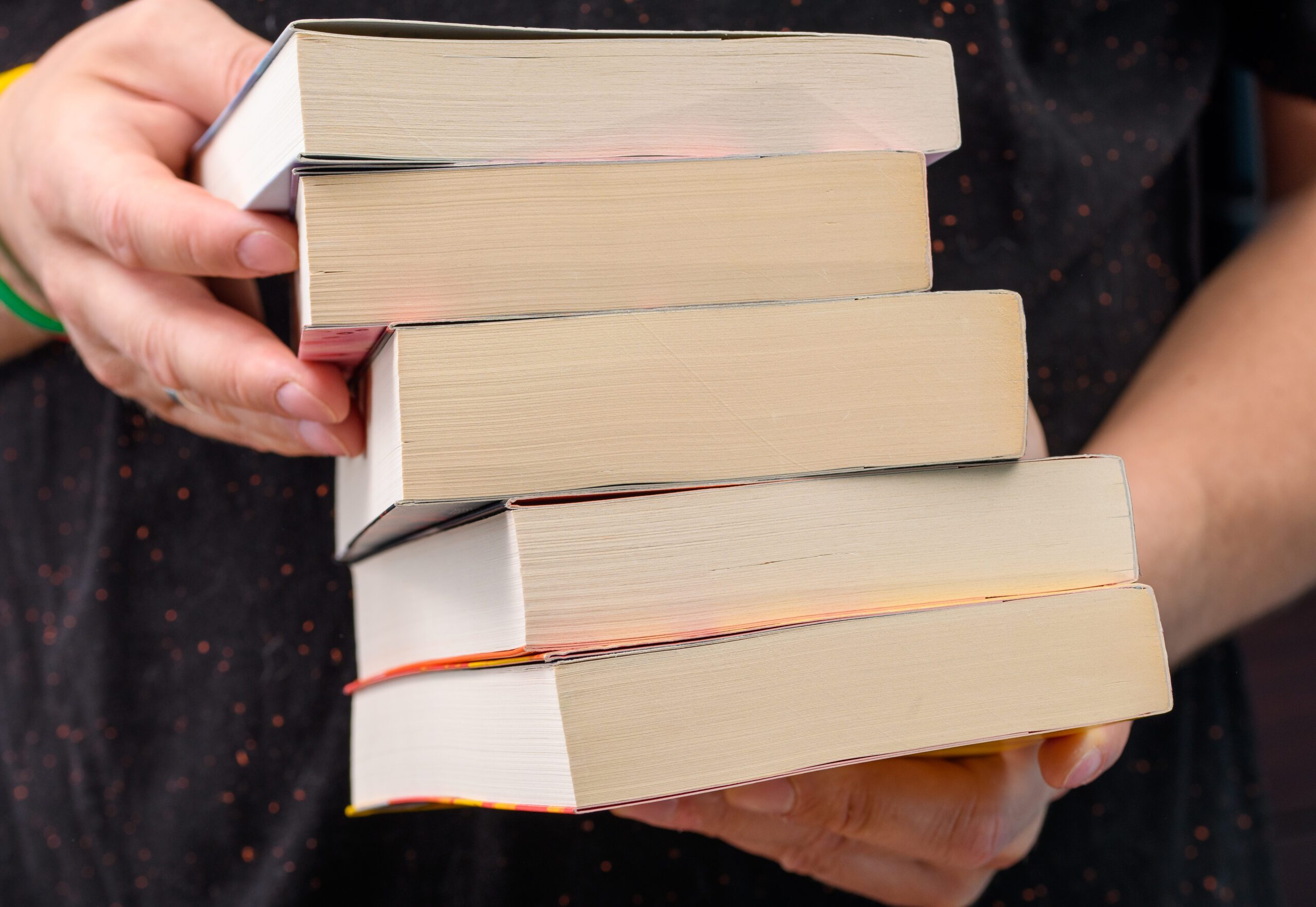 A man holding a stack of books in his hands, closeup